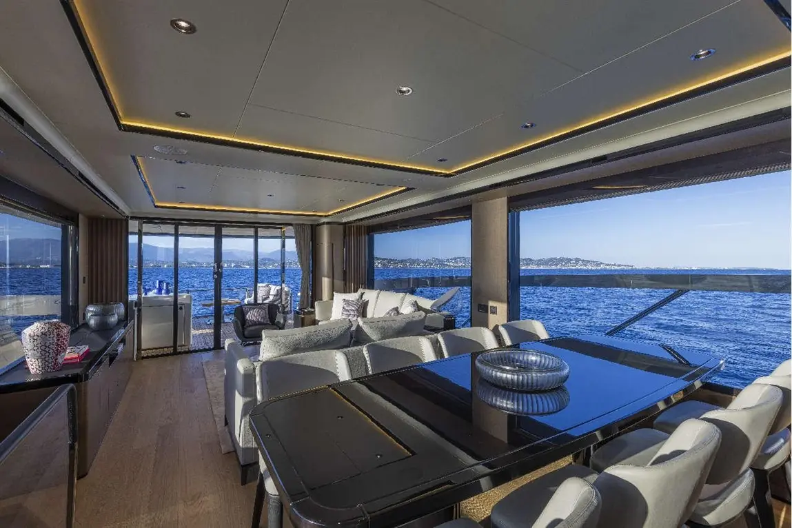 Luxurious yacht interior featuring a sleek dining table, comfortable seating, and panoramic sea views through large windows.